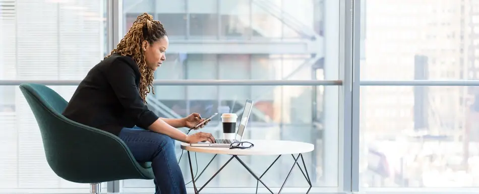 woman sitting in office building looking at computer and phone