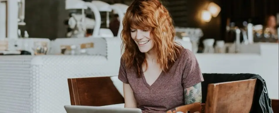 A woman smiling and looking at their laptop.