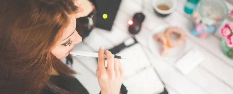A woman thinking with a pen in her mouth.