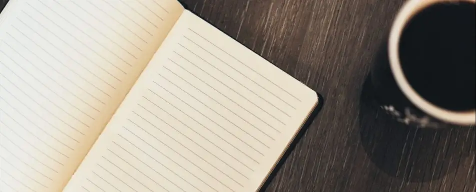 A blank open notebook with a cup of coffee next to it.
