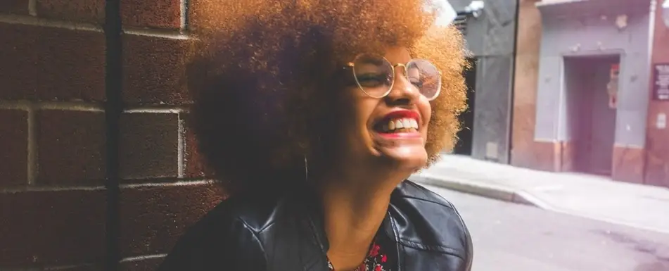 A Black woman in a leather jacket and glasses smiling.