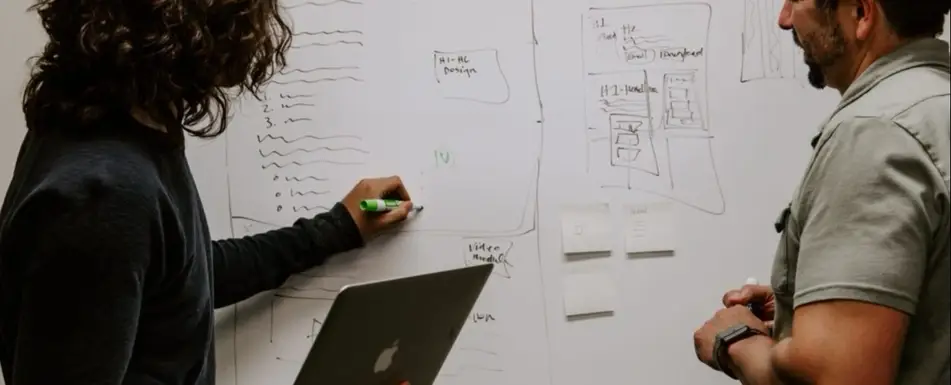 Two people writing on a whiteboard.