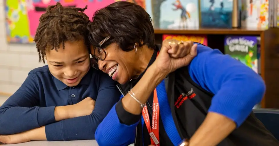 Black woman volunteers with AARP Foundation Experience Corps to support a young child with reading skills.