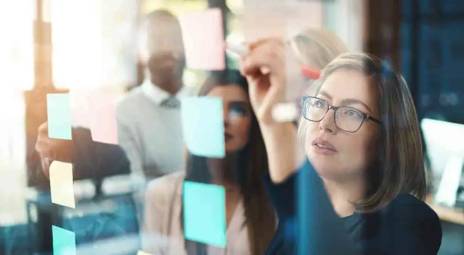 Mujer escribe en notas adhesivas sobre cristal con su equipo de fondo