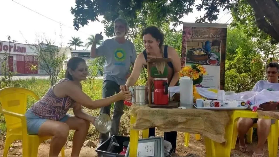 Imagen de cuatro personas: una mujer sirviendo café a otra, un hombre con una camiseta de Idealist y otra mujer sentada en la esquina de la mesa