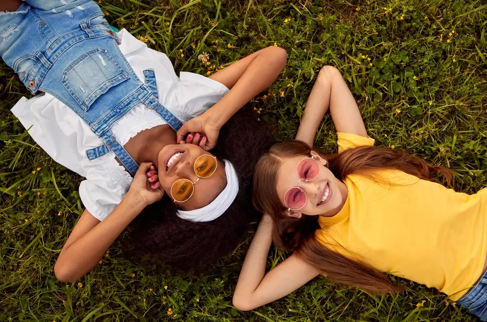 two girls smile at camera while lying on the grass