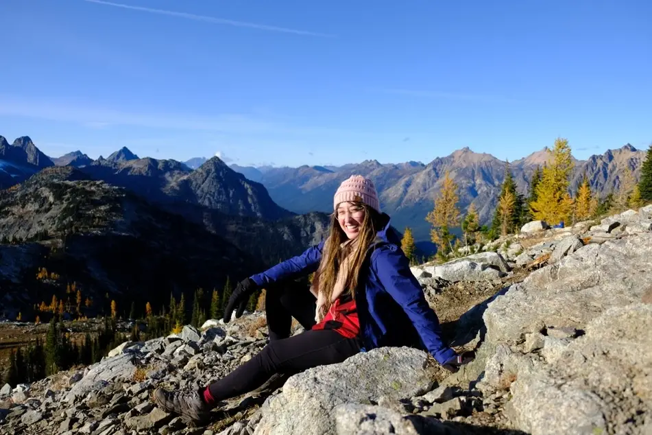 A photograph of Sara Vasquez sitting with a blue sky above and other mountains behind her.