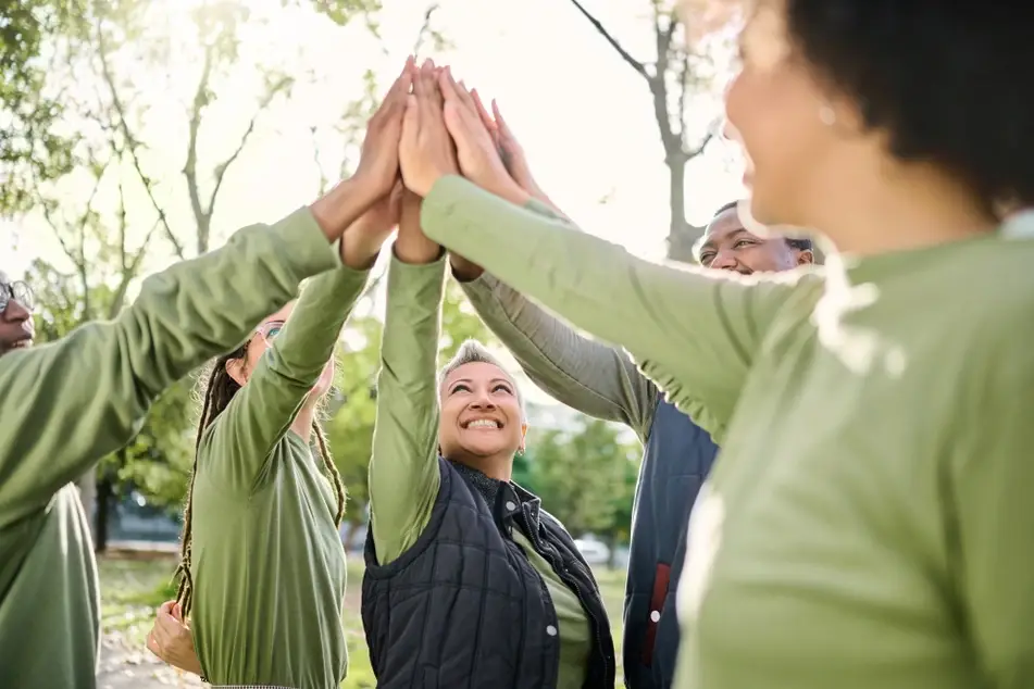 a group of volunteers wearing long sleeve green shirts smile and high five outside