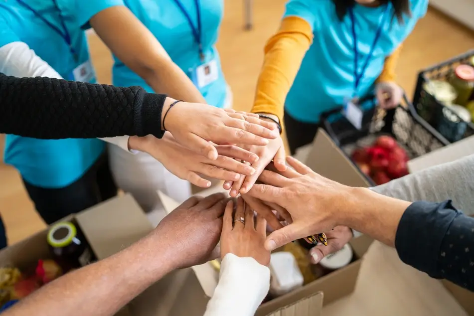 volunteers stacking hands together over donations in boxes