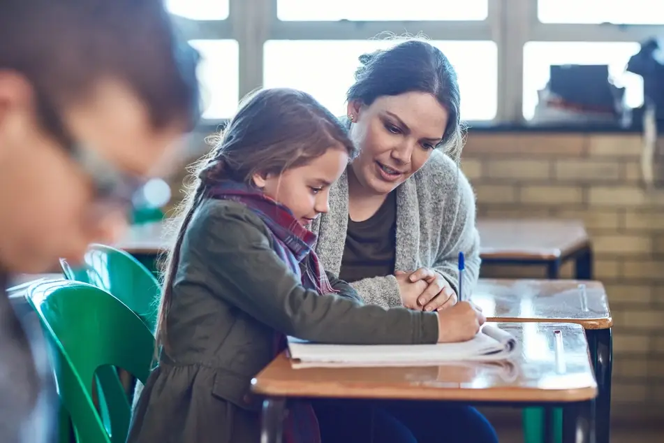 A volunteer teacher helps a little girl with her homework at school.
