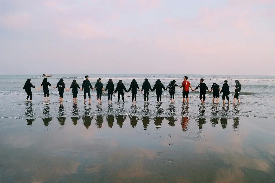 Grupo de personas tomándose de las manos en la orilla del mar