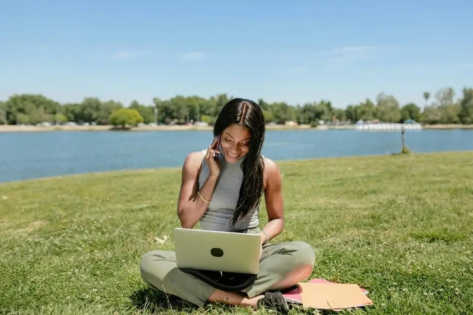 A woman using a laptop while sitting on grass