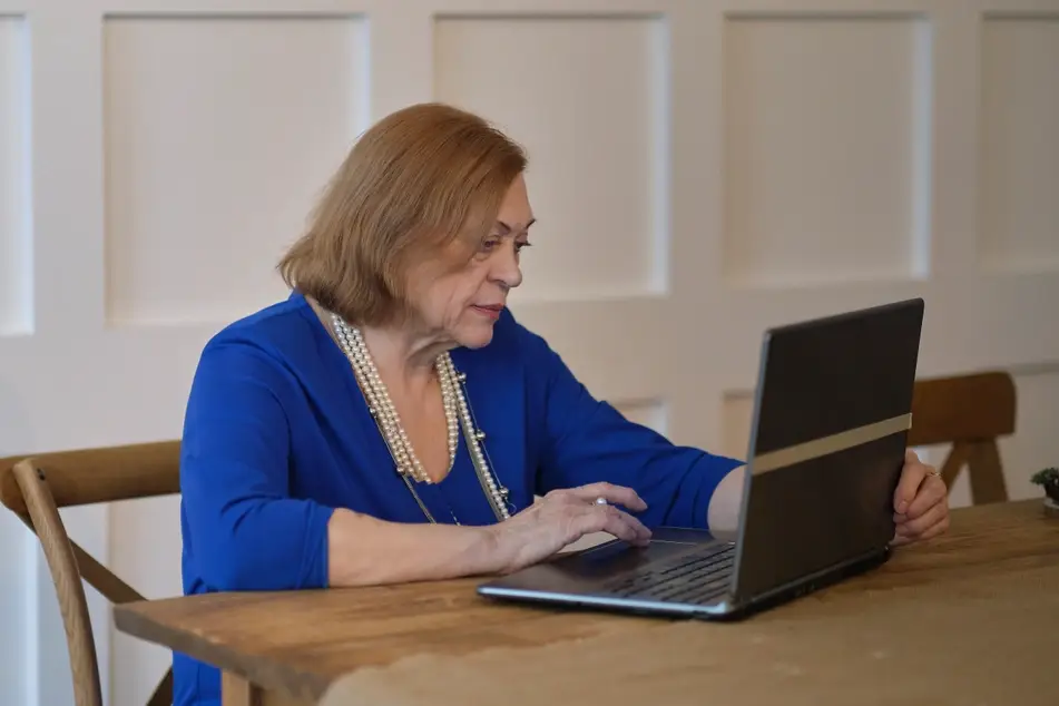 Older white woman looks at website on laptop in her home