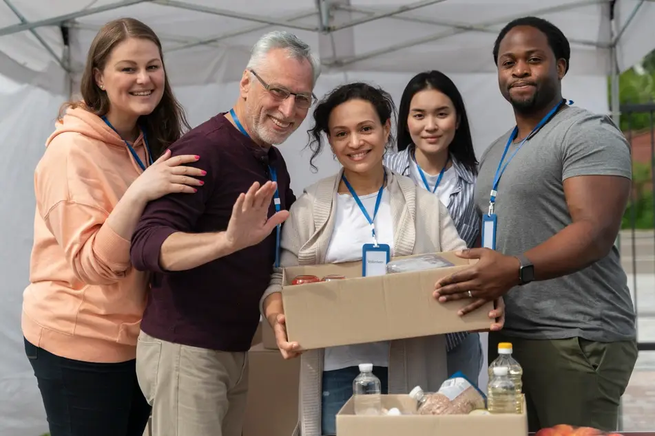 Foto de 5 pessoas voluntárias posando para a foto com a mulher ao centro segurando uma caixa com alimentos