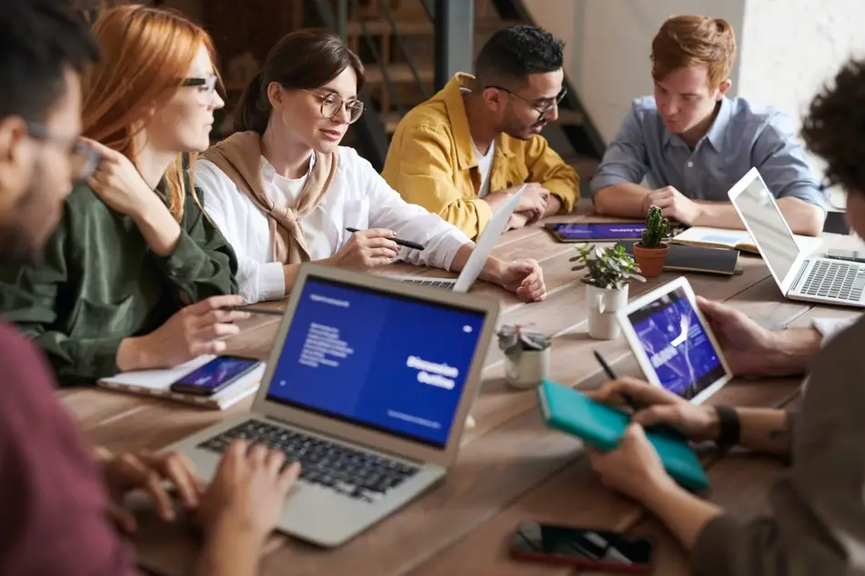 Grupo de personas mirando las pantallas de sus computadoras alrededor de una mesa de madera