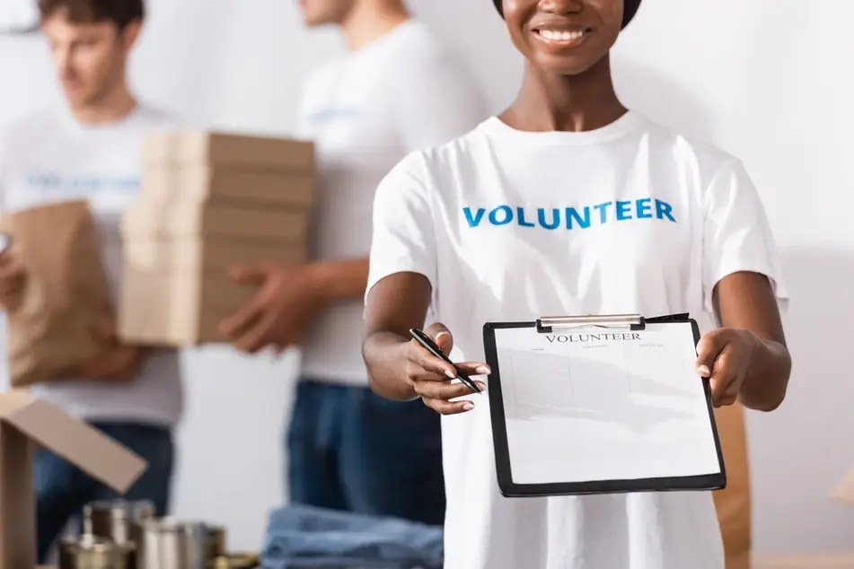 Volunteer smiles while holding out a sign-up form at a nonprofit organization.