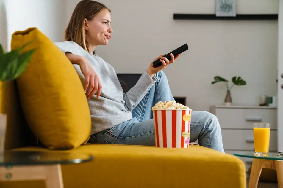 Woman in living room watching movie about volunteering with popcorn