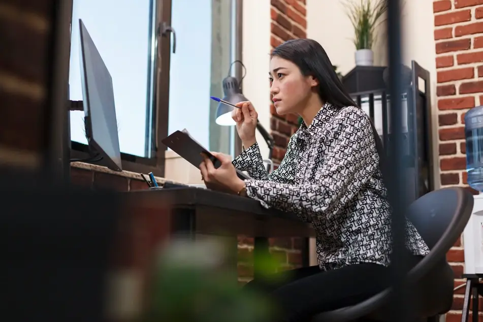Asian woman with long hair looks intently at computer screen at the office