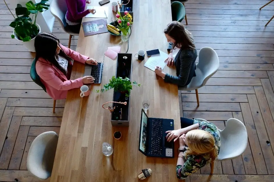 3 mujeres sentadas en un escritorio en una oficina con computadoras