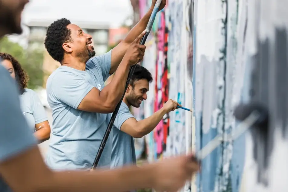 People smiling and painting an outdoor mural