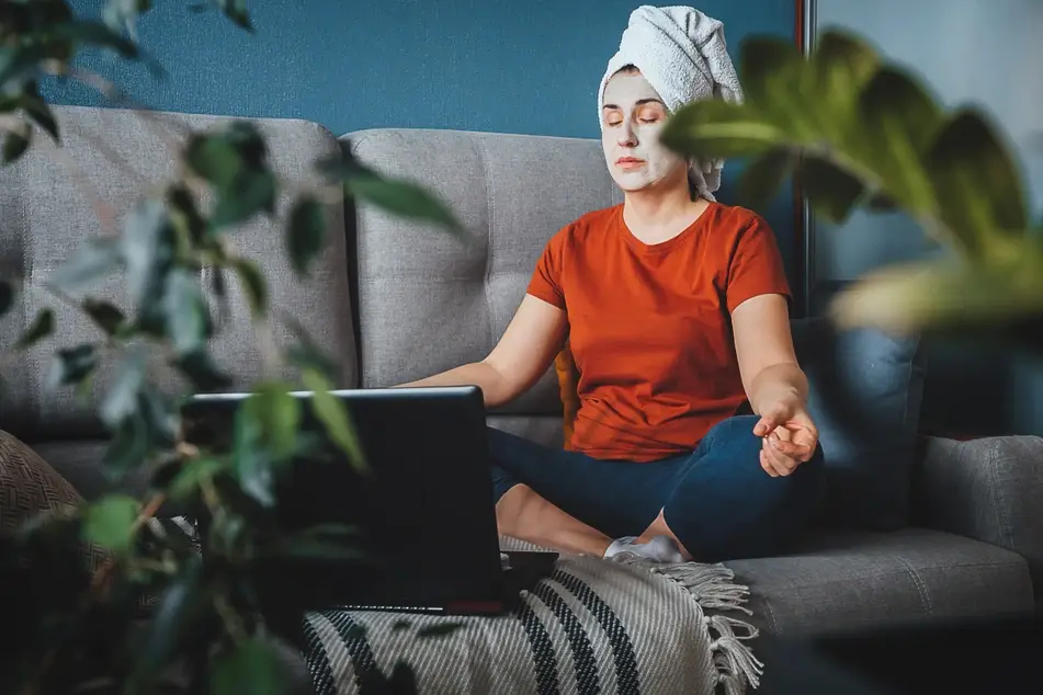 Woman sits on couch with hair up and face mask on practicing self care