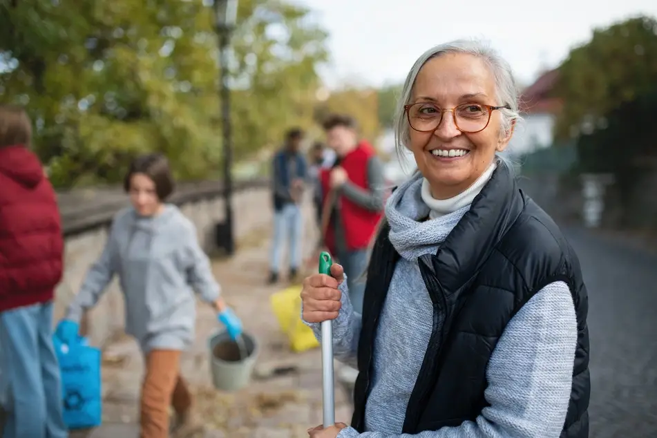 Older woman holding a broom smiles while volunteering with her membership-based organization