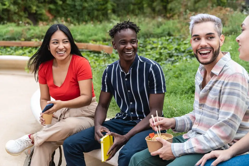 A photograph of various co-workers sitting outside eating lunch and laughing.