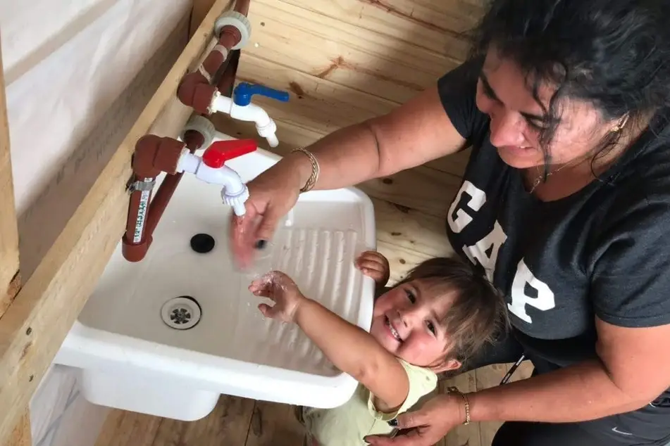 Mujer ayudando a su hija a lavarse las manos en un lavabo.