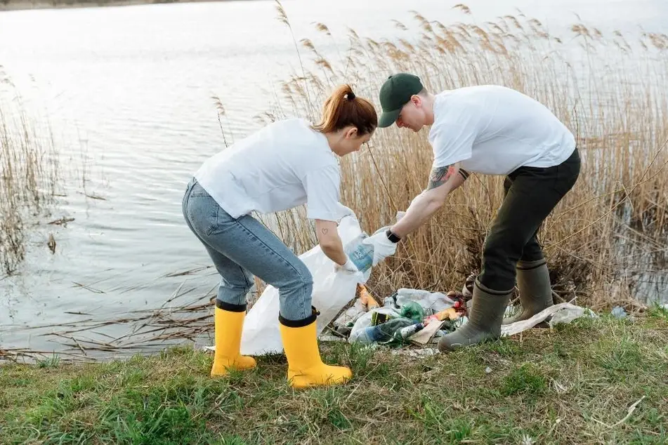 Personas recogen basura a la orilla de un lago.