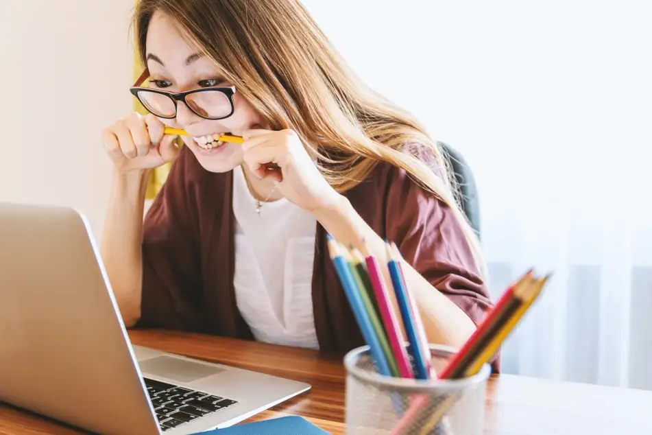 Mujer estresada mordiendo un lápiz frente a su computador