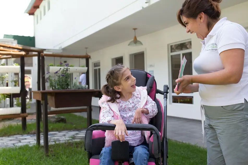 Niña con parálisis cerebral en silla de ruedas, sonriendo mientras trabaja en una terapia