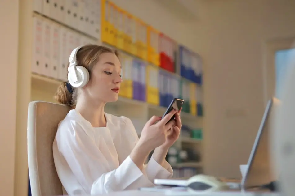 woman looking at cell phone while sitting at laptop