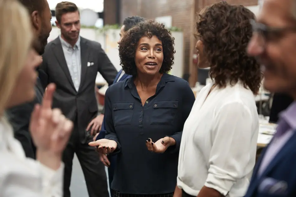 Group of co-workers networking at the office, two Black women talking to each other.