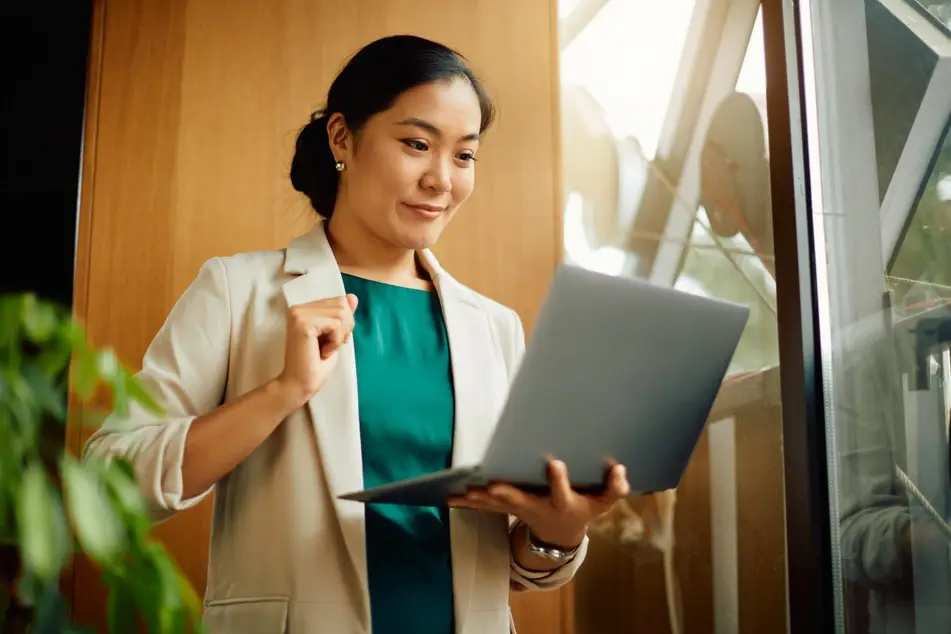 Woman stands and smiles at laptop while publishing a LinkedIn profile online