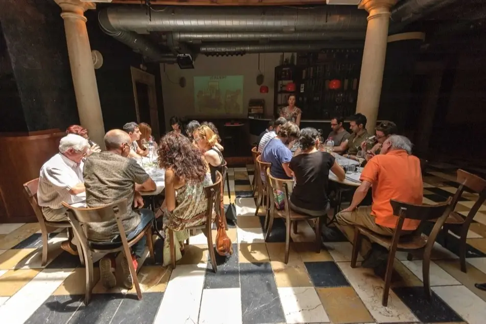 Personas reunidas en mesas de un bar escuchando a alguien