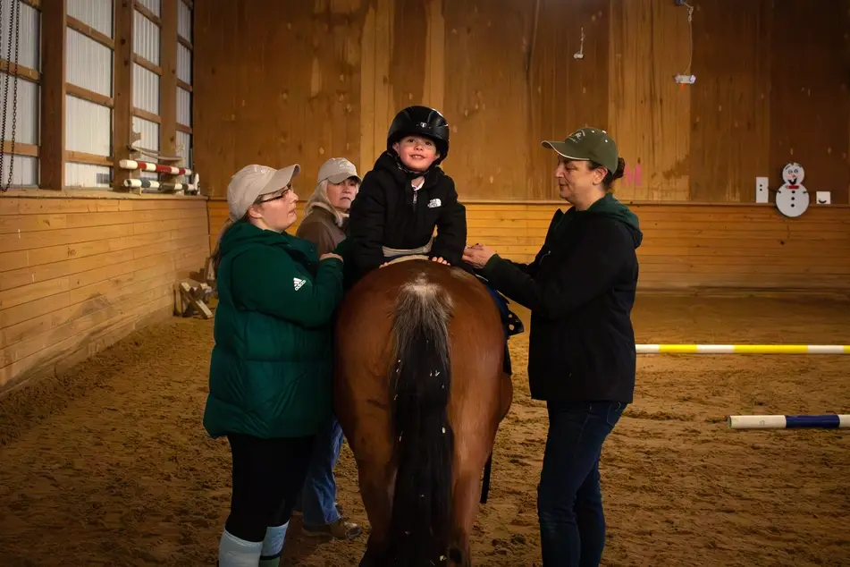 Volunteers support a young boy with learning to ride a horse at Ridgebury Riders in Connecticut