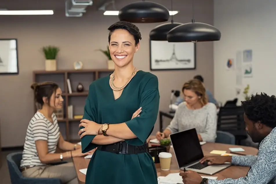 smiling woman standing at foreground of table where people are working