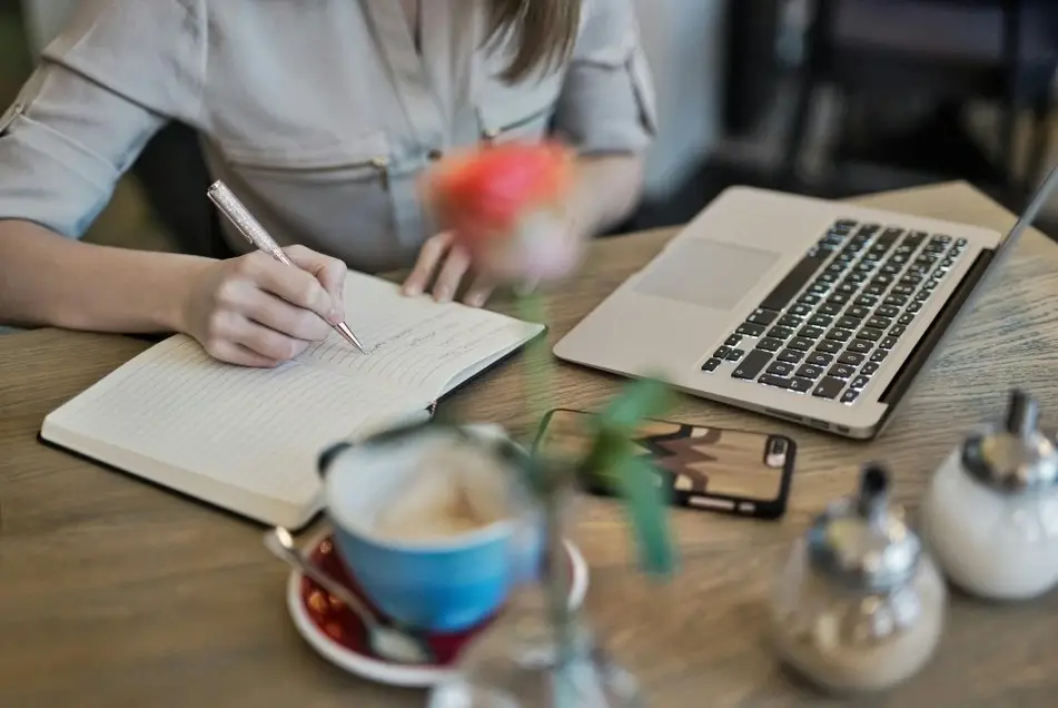 Mujer escribiendo en un cuaderno de notas junto a una laptop