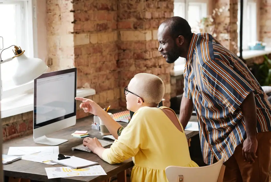 White woman with cancer sits at desk next to Black co-worker.
