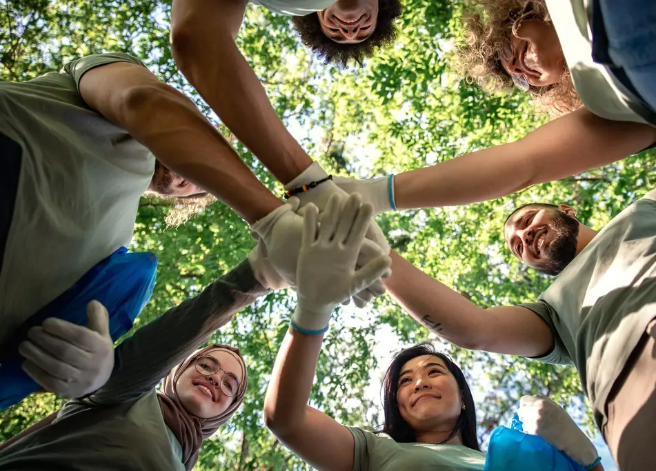 a group of co-workers volunteer together and put their hands together after completing their volunteer opportunity cleaning up a local park
