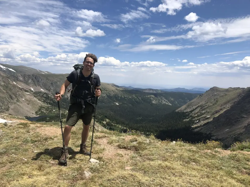 A photograph of James Warren hiking, with blue skies and mountains behind him.