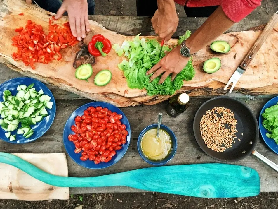 Grupo de personas cocinando sobre una tabla llena de ingredientes.